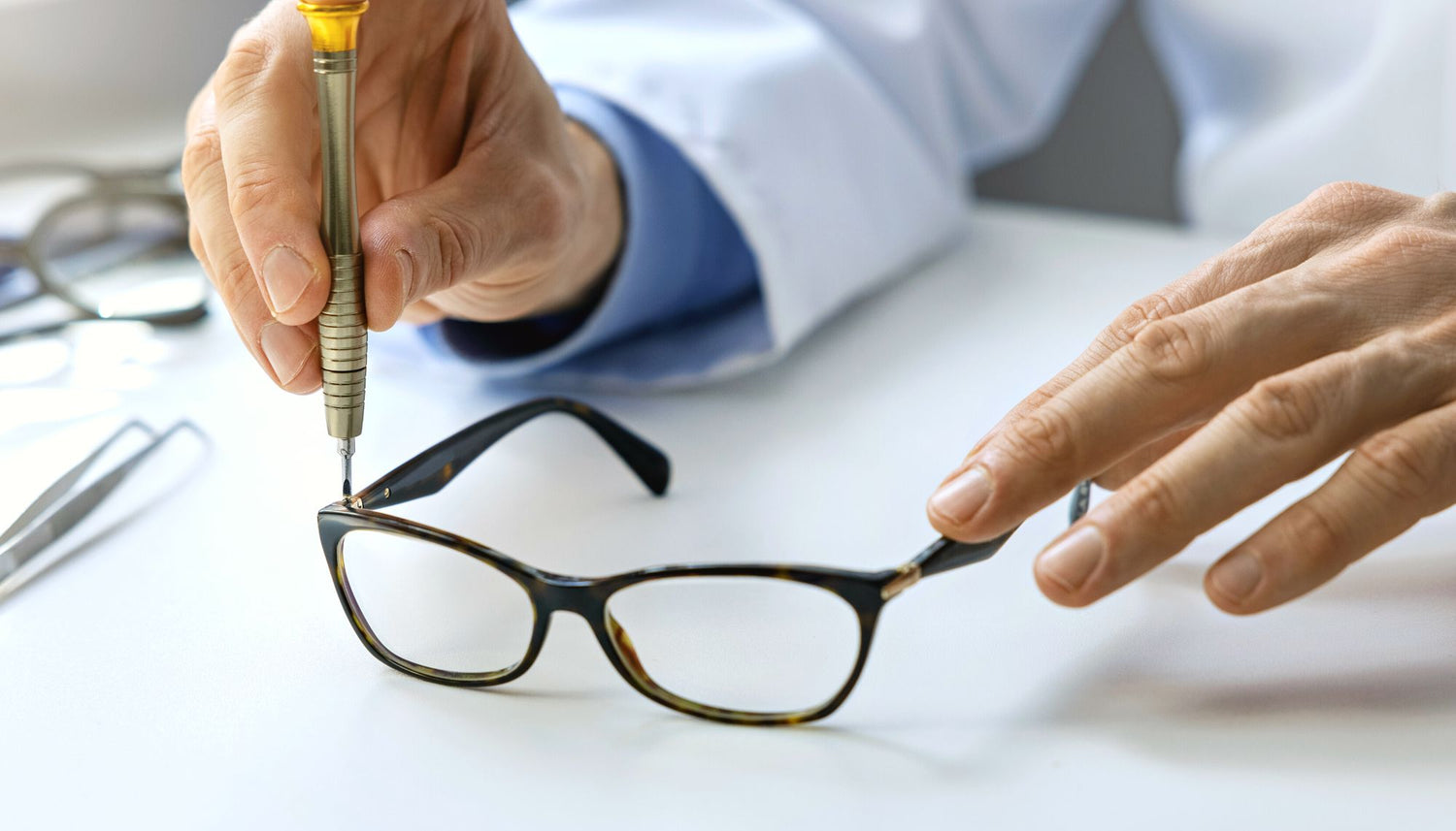 Hands repairing black glasses with a screwdriver. 