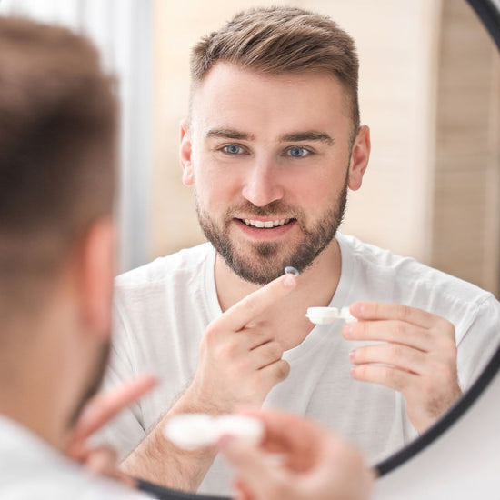 Man looking in mirror while inserting a contact lens. 